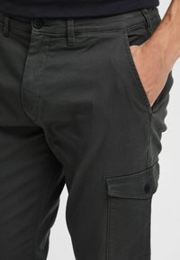 Dark gray cargo pants, featuring a front pocket, a side cargo pocket with button closure, smooth texture, and a fitted design.