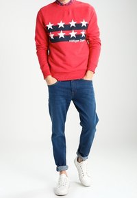 Sudadera roja con estrellas blancas y franjas azul marino, combinada con vaqueros azul claro y zapatillas blancas. Diseño sencillo con cuello redondo.