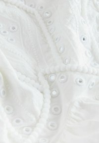 Tissu blanc avec des motifs ajourés brodés et une chaîne de perles blanches rondes drapée dessus.