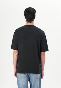 Schwarzes Baumwoll-T-Shirt mit lässiger Passform, kurzen Ärmeln und geripptem Rundhalsausschnitt, kombiniert mit hellblauen Jeans.