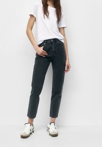 Tummanharmaat korkea vyötäröiset farkut, joissa on suora leikkaus ja hienovarainen haalistunut pinta, yhdistetty valkoiseen pyöreäkaulaiseen t-paitaan ja valkoisiin lenkkareihin.