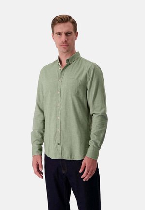 Camicia verde chiaro con bottoni, realizzata in tessuto testurizzato, dotata di una tasca sul petto, maniche lunghe e bottoni in contrasto. Indossata con jeans scuri.