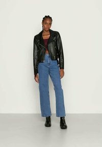 Jaqueta de motoqueiro em couro preto com zíperes prateados, combinada com um top cropped bordô e jeans retos azuis. Botas de tornozelo pretas completam o visual.