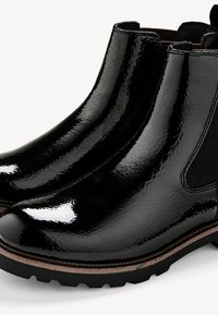 Bottes Chelsea en cuir noir brillant avec panneaux latéraux élastiques et semelles robustes marron et noires.