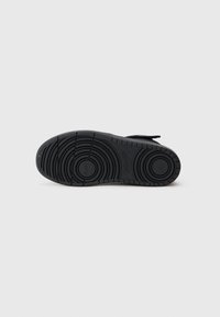 Sola de sapatilha preta com padrões de rasto circulares e logótipo da Nike, mostrada de baixo sobre um fundo branco.