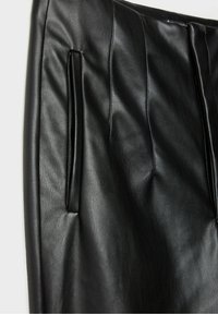 Zwarte leren rok met een zachte textuur, voorzien van plooien aan de voorkant en zijzakken. Close-up toont de glans en details van het materiaal.
