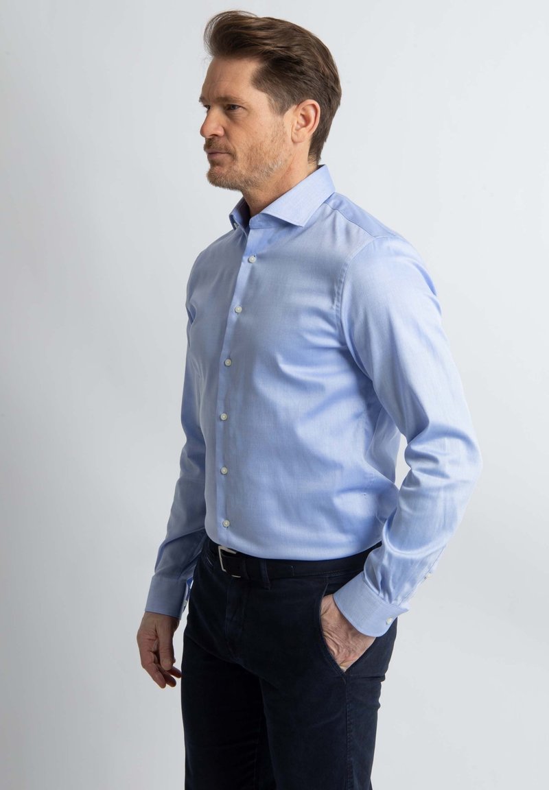 Lichtblauw button-up shirt gemaakt van een gladde stof, met een klassieke kraag en lange mouwen, gecombineerd met donkere broeken.