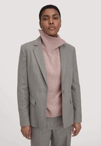 Grijze blazer over een roze geribbelde coltrui, met een dubbele knoopsluiting, gelapteloten en een op maat gesneden pasvorm.