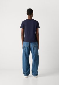 T-shirt di cotone blu navy con maniche corte, abbinato a pantaloni cargo in denim blu chiaro a vestibilità ampia, dotati di tasche laterali e dettagli di cucitura.