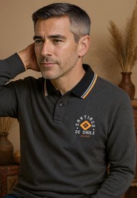 Donkergrijze lange mouw polo met een zwarte kraag, oranje strepen en geborduurd "Santiago de Chile" logo op de borst.