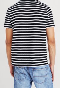 Czarna i biała koszula w paski z krótkim rękawem i prążkowaną fakturą, zestawiona z niebieskimi dżinsami z tylnymi kieszeniami.