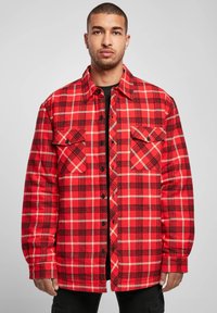 Red and black plaid flannel shirt with two chest pockets, black buttons, and long sleeves. The fabric exhibits a soft texture.