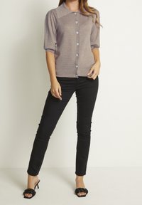 Cardigan color marrone chiaro con un motivo testurizzato, maniche a sbuffo corte e chiusura con bottoni, abbinato a pantaloni skinny neri e sandali neri con tacco.