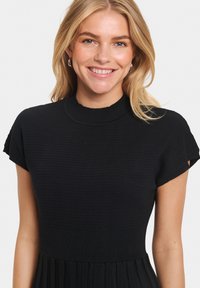 Black knit dress with a ribbed texture, short sleeves, high neckline, and a pleated skirt design. The fabric appears soft and stretchy.