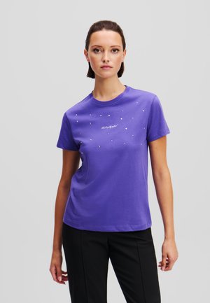 Tricou din bumbac mov, cu mâneci scurte, având embellishementuri argintii și un design grafic alb pe față.