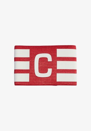 Červená kapitánska páska s veľkým bielym písmenom „C“ uprostred a tromi bielymi horizontálnymi pruhmi na každej strane.