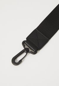 Sangle en textile noire avec un système de fixation solide et un accent en cuir avec un motif triangulaire embossé, texture textile évidente.