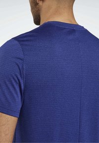 Modré tričko s krátkými rukávy, které má texturovaný vzor a kulatý výstřih; látka působí prodyšně a má hladký povrch.