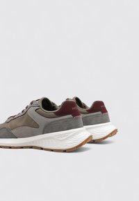 Un paio di sneakers grigie e marroni con suole bianche texture e accenti di tacco color marsala, posizionate affiancate con la parte posteriore rivolta verso l'esterno su uno sfondo semplice.