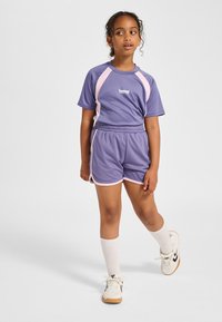 Lila sportset med en kortärmad topp med rosa detaljer och matchande shorts. Inkluderar vita knähöga strumpor och sneakers.