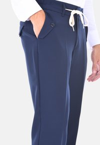 Pantaloni blu navy realizzati in tessuto liscio con vita regolabile tramite cordoncino e tasche laterali, caratterizzati da un dettaglio a bottone sulla tasca.