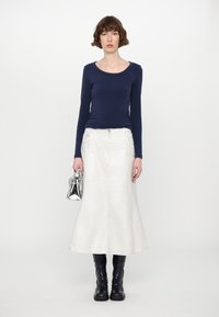 Top a maniche lunghe blu navy, gonna di jeans a campana bianca, stivali neri fino al ginocchio e una borsa in argento. Texture morbide e colori in contrasto.