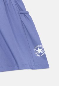 Μωβ ύφασμα με απαλή υφή που διαθέτει πλαϊνή τσέπη. Περιλαμβάνει λευκό κυκλικό λογότυπο με αστέρι και κείμενο "CONVERSE ALL STAR".