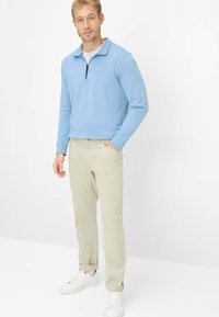 Maglione azzurro a maniche lunghe con collo con zip, abbinato a pantaloni beige e scarpe da ginnastica bianche. Tessuto liscio; vestibilità casual e moderna.