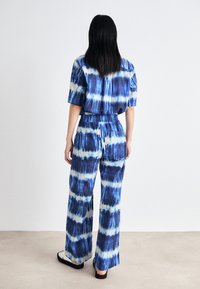 Ensemble assorti en tie-dye bleu comprenant un haut à manches courtes et un pantalon à jambes larges. Tissu doux avec une taille élastique, présentant un motif ondulé.
