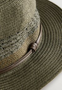 Sombrero trenzado de paja verde olivo con ala ancha, decorado con una banda de cuero marrón suave. Presenta un patrón texturizado en la corona.