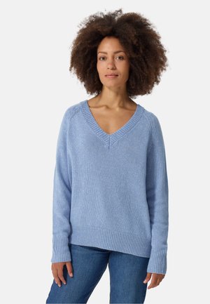 Hellblaues gestricktes Sweatshirt mit V-Ausschnitt, gerippten Bündchen und Saum. Der Stoff hat eine subtile Textur und eine entspannte Passform. Getragen über Jeans.