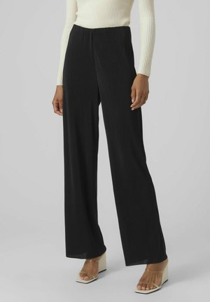 Zwarte, hooggesneden wijde broek met verticale ribbelstructuur. Gecombineerd met een aansluitend crèmekleurig longsleeve top en transparante blokhak sandalen.