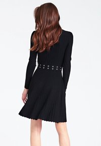 Robe noire côtelée à manches longues, taille cintrée et ourlet festonné. Comprend une ceinture avec des œillets circulaires. Tissu texturé.