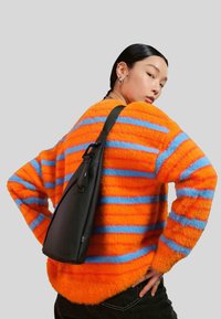 Borsa nera a spalla posizionata su un maglione morbido a strisce arancioni e blu. La borsa presenta un design elegante con una finitura testurizzata e una tracolla regolabile.