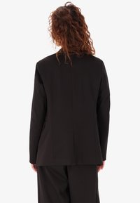 Blazer nero su misura con un design strutturato, con una fessura centrale sul retro e maniche lunghe; realizzato in un tessuto liscio e testurizzato.