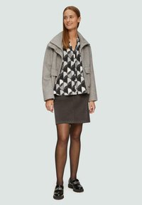 Veste en laine grise avec un grand col sur une chemise à motif noir et blanc, associée à une jupe gris foncé et des mocassins noirs brillants.