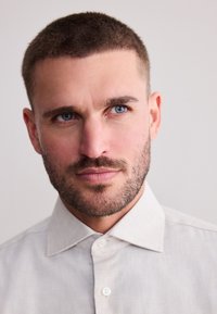 Chemise gris clair à boutons avec un col pointu et une texture subtile. Portrait en gros plan d'un homme aux cheveux courts et aux yeux bleus.