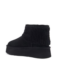 Crne čizme do gležnja s glatkom sukanom gornjištem i rebrastim pletenim rubom. Imaju debeli platformasti potplat za dodatnu visinu i udobnost.