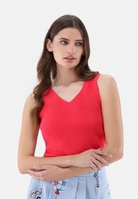 Rotes geripptes Tanktop mit V-Ausschnitt, ausgestattet mit schmalen Trägern und einer taillierten Silhouette, kombiniert mit einem hellblauen Rock mit Mustern.