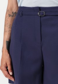 Skräddarsydda marinblå byxor med en slät textur, med flat front, bältesloopar och en silverfärgad spänne detalj i midjan.