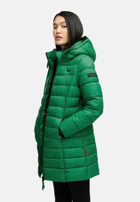 Parka imbottita verde con cappuccio, caratterizzata da un design trapuntato e dettagli rossi. Il materiale è liscio, con chiusura a zip e tasche laterali.