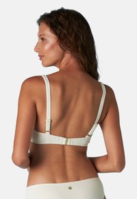 Reggiseno in tessuto avorio con spalline regolabili e dettagli in metallo dorato. Presenta una fascia liscia e un design minimalista.