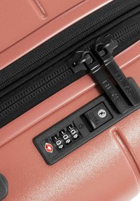 Rose-colored suitcase with a textured surface, featuring dual black zippers and a combination lock with a keyhole for security.