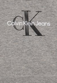 Felpa grigia in cotone con un grande logo nero "K" e il testo bianco "Calvin Klein Jeans" sottostante. Texture liscia con un sottile motivo mélange.