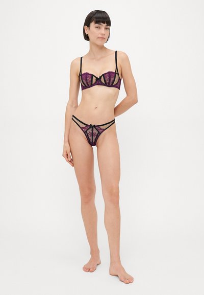 Lingerie set featuring black lace with purple details, underwire bra with sheer panels, and matching thong with crisscross straps and bow accents.