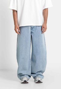 Jasnoniebieskie dżinsy typu wide-leg o luźnym kroju, zakończone klasycznym zapięciem na guziki i zamek błyskawiczny. Połączone z luźną białą koszulką.