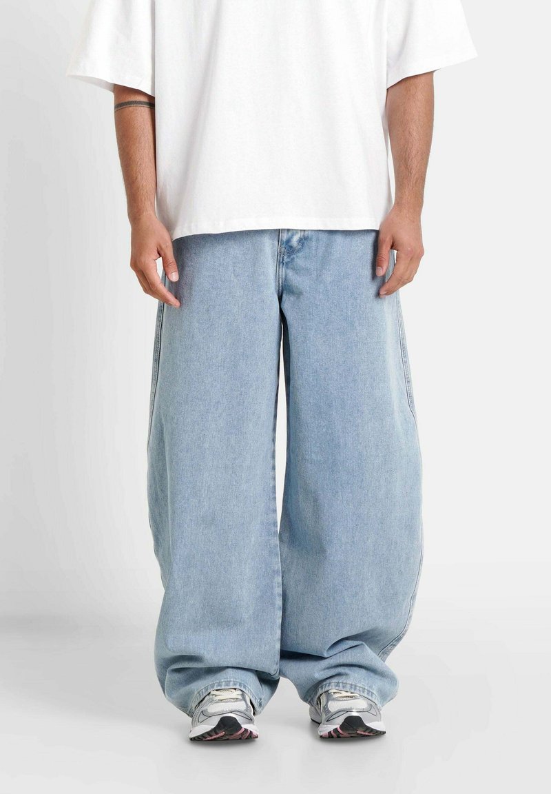 Jasnoniebieskie dżinsy typu wide-leg o luźnym kroju, zakończone klasycznym zapięciem na guziki i zamek błyskawiczny. Połączone z luźną białą koszulką.