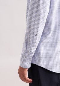 Camicia a quadri azzurri con maniche lunghe, polsini con un bottone e dettaglio del logo ricamato sulla manica. Materiale in cotone.