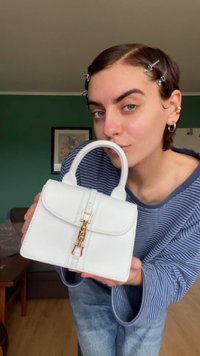 Bolsa estruturada branca feita de material sintético, com uma alça superior, ferragens douradas e detalhes em costura.