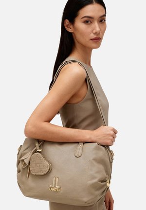 Borsa a mano in pelle beige con dettagli in oro. Presenta una forma curva, un ciondolo a forma di cuore e un design trapuntato. Include una tracolla.